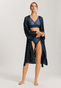 Navy blauwe kanten bralette en slipje, gecombineerd met een lange, gebloemde satijnen ochtendjas. De jas heeft bloemenpatronen en brede mouwen.