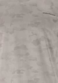Ljusgrå träningsskjorta med ett subtilt kamouflage-mönster, tillverkad av andningsbart tyg med fin textur, märkt med "ENDURANCE."