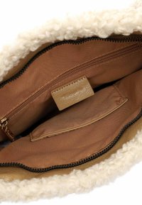 Borsa marrone con cuciture a contrasto e bordo in soffice pelliccia bianca. Presenta una chiusura con zip e una tasca interna con etichetta in pelle. Texture morbida in tutta la superficie.