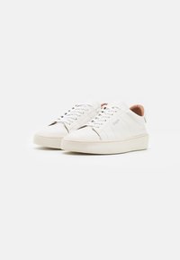 Sneakers bianchi in pelle con profilo basso, punta arrotondata e suola bianca texturizzata. Lacci e sottile dettaglio del logo sul lato.