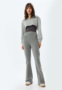 Sudadera gris corta sobre una camiseta negra, combinada con pantalones acampanados grises. Hecha de un material suave con una textura lisa. Zapatillas blancas.