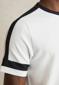 Hvid tekstureret kortærmet t-shirt med navy ribbet krave og skulderdetaljer, der fremhæver et sporty design.