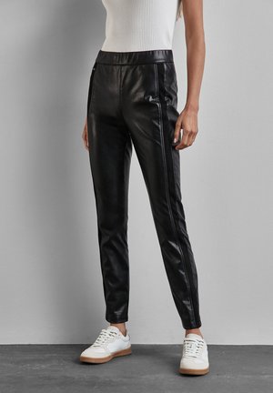 Zwarte leren broek met een slanke pasvorm, elastische tailleband en contrasterende zijnaad. Draag het met witte sneakers op een gestructureerde vloer.