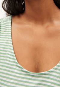 Chemise en coton rayée verte et blanche avec un col arrondi, affichant une texture de tissu douce et des coutures visibles le long des bords.