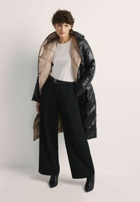 Czarna kurtka puchowa z beżowym wnętrzem, dużym kapturem i pikowanym wzorem. Połączona z białą bluzką, szerokimi czarnymi spodniami i botkami za kostkę.