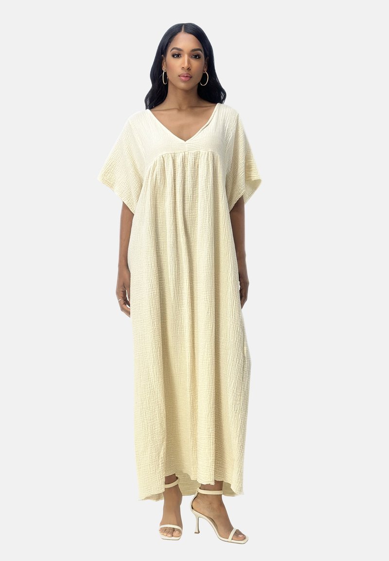 Robe maxi beige clair en tissu texturé, avec un décolleté en V, des manches larges et une coupe fluide, assortie à des sandales à talons neutres.
