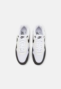 Tenisi Nike alb-negru cu partea superioară din plasă și material sintetic, vârf rotund, șireturi plate și logo-ul caracteristic swoosh pe laturi.