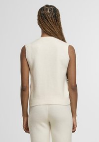 Maglione senza maniche color crema con orlo a coste e una texture morbida, progettato per una vestibilità rilassata, con un retro liscio senza decorazioni.