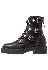 Stivale in pelle nera alla caviglia con suola spessa, tre cinturini con fibbia decorati con perle bianche e borchie argentate nell'area del tacco.