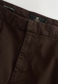 Braune schmal geschnittene Hose aus glattem Material mit einer gesteppten Taille und seitlichen Taschen. Markenlabel innen sichtbar.