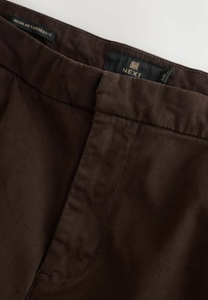 Braune schmal geschnittene Hose aus glattem Material mit einer gesteppten Taille und seitlichen Taschen. Markenlabel innen sichtbar.