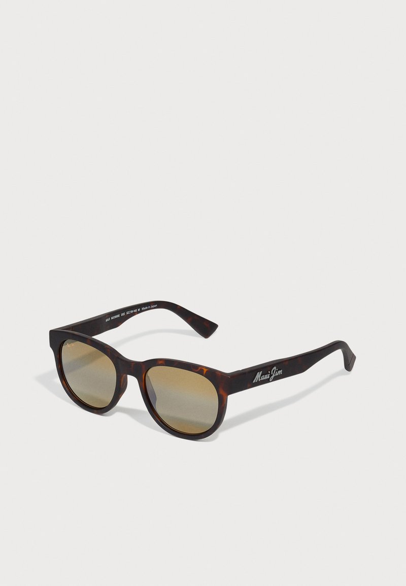 Lunettes de soleil écaille de tortue avec verres marron, forme rectangulaire et monture épaisse. Présente un logo sur le côté. Matériau plastique léger.