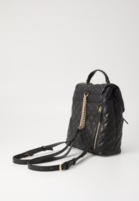 Mochila de cuero acolchado negro con detalles en dorado en la cremallera y la cadena, correas ajustables y asa superior sobre fondo blanco.