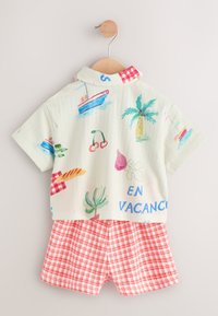 Short-sleeve, pastel green shirt with tropical prints and "EN VACANCES" text, paired with red and white checkered shorts. Cotton blend.