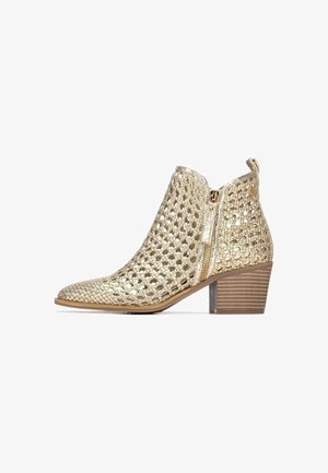 Botín tobilleros dorado tejido con punta puntiaguda, cierre lateral con cremallera y tacón apilado. Presenta un diseño de malla abierta para un aspecto texturizado.