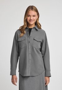 Grijze geknoopte shirt met twee borstzakken, gemaakt van een gestructureerde stof. Lange mouwen en een afgeronde zoom, met metalen drukknoopknopen.