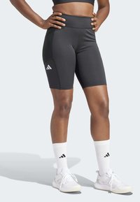 Pantalones cortos deportivos negros con una cintura alta, con un logo blanco de Adidas en el lateral. Tejido suave y elástico, diseñado para la comodidad.