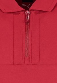 Czerwona bluza z zamkiem błyskawicznym i kołnierzem. Gładka tekstura materiału i widoczne szwy wzdłuż zamka. Posiada małe logo w pobliżu dekoltu.