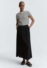 T-shirt a righe bianche e nere, gonna maxi nera con cintura elastica e sandali neri con accessori decorativi. Tessuto di consistenza liscia.