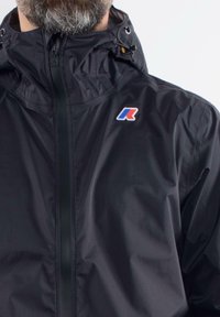 Black lightweight jacket with a high collar, features a zipper front, drawstrings, and a multi-colored logo on the left chest.