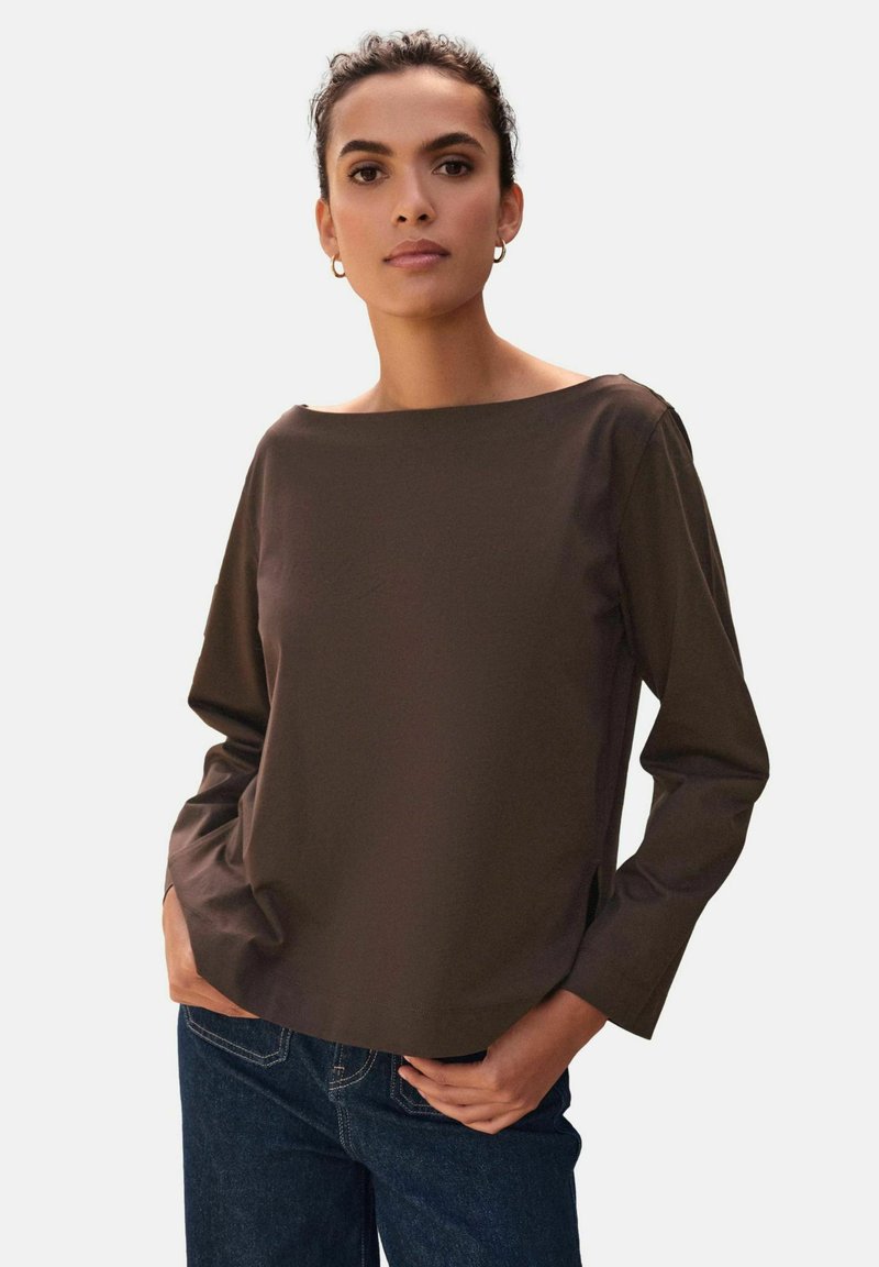 Maglia marrone a maniche lunghe con scollo a barca, realizzata in tessuto liscio, con vestibilità comoda e spacchi laterali, abbinata a jeans in denim scuro.