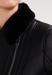 Svart läderjacka med en mjuk svart pälskrage, silverdragkedja och en texturerad yta med strukturerade sömmar.