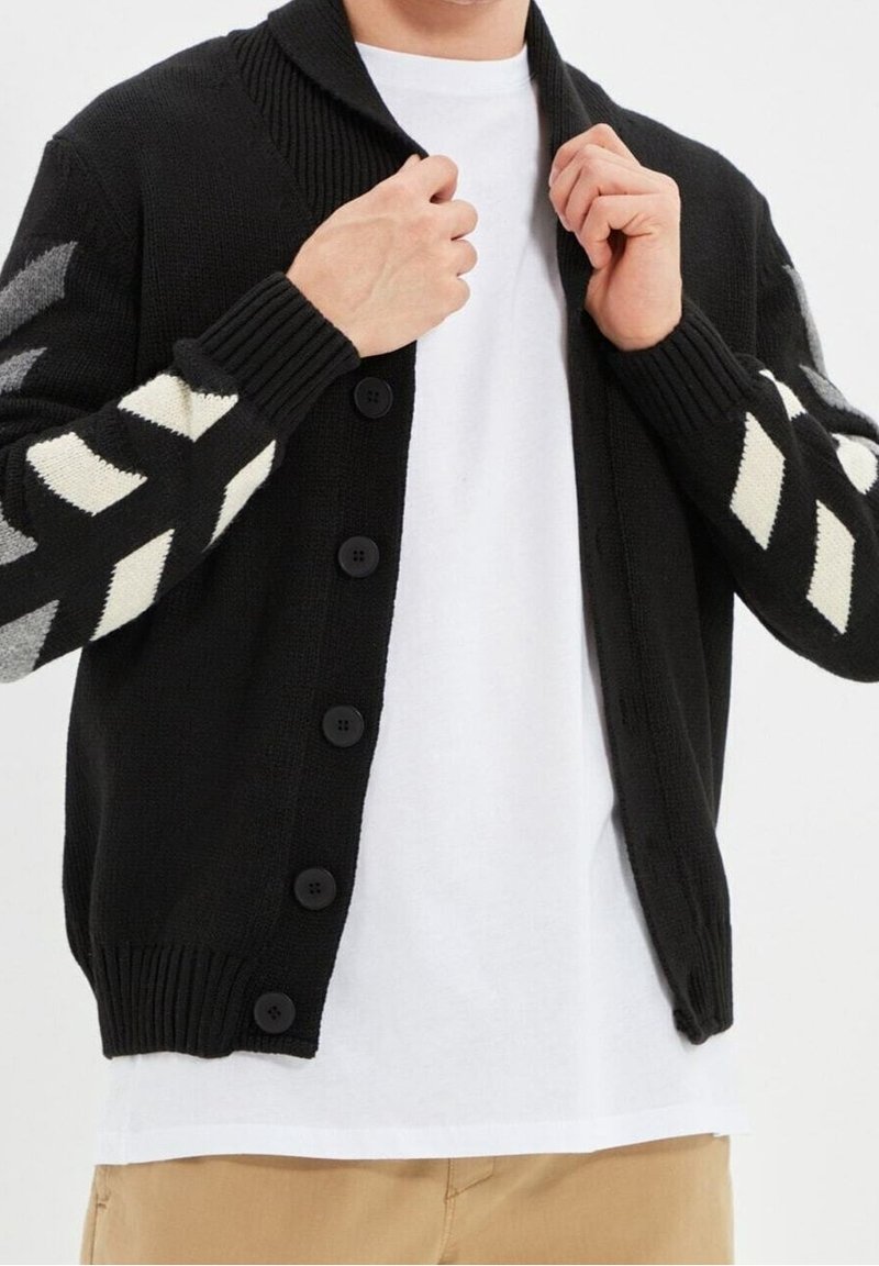 Cardigan nero in maglia con colletto a coste, dotato di grandi bottoni neri e maniche patterned con disegni zigzag in crema e grigio.