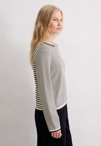 Schwarz-weiß gestreiftes Langarmshirt mit Rundhalsausschnitt, weicher Stoff und gerippten Bündchen, kombiniert mit dunklen Hosen, seitlich betrachtet.