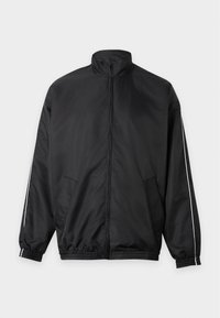 Veste noire zippée intégralement avec col montant, poignets et ourlet élastiques, poches latérales et fines bandes blanches le long des manches.