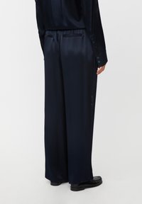 Pantalones de pierna ancha en azul marino, fabricados en un tejido suave y brillante, con un pliegue en la parte posterior y dos bolsillos. Presentan una cintura ajustada y una silueta elegante.
