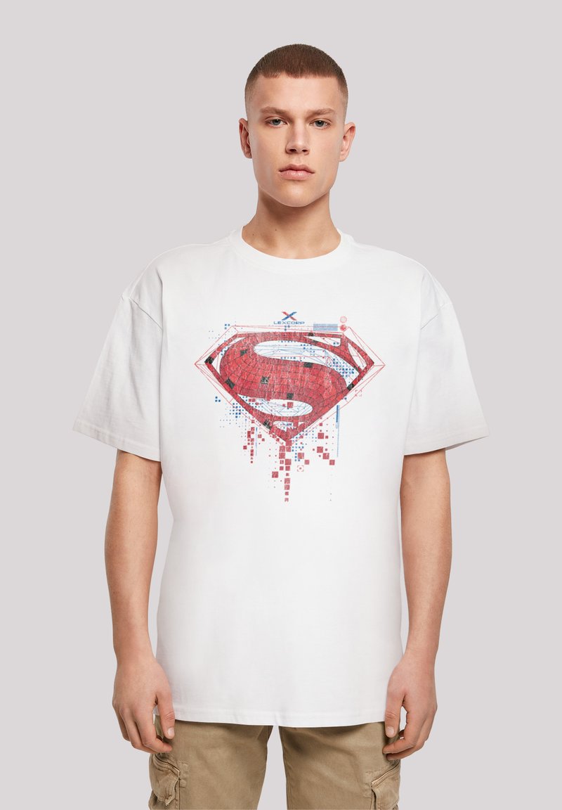 Hvit bomulls-T-skjorte med et stort rødt og blått Superman-logo grafikk, med pikselerte og abstrakte detaljer. Korte ermer, rund hals.