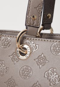 Geantă de umăr gri deschis, cu modele florale embossate, două curele și un detaliu cu logo de culoare aurie pe un accent din hardware circular.