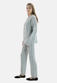 Pull en maille torsadée gris et pantalon assorti, présentant des motifs texturés. Le modèle porte des ballerines noires, et la tenue a une coupe décontractée.