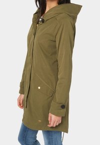 Olivově zelená voděodolná parka s kapucí, předním zipem, dvěma bočními kapsami a knoflíkovými detaily. Hladká textura a délka ke kolenům.