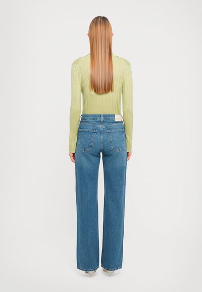 Light green ribbed long-sleeve top paired with high-waisted wide-leg blue jeans. Notable back pockets and minimalistic design details.