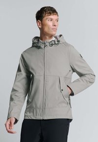 Lichte, grijze, waterdichte jas met een capuchon, verstelbare koordjes, meerdere zakken en een ritssluiting aan de voorkant.