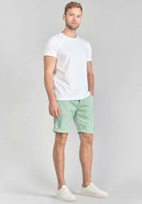 T-shirt blanc à manches courtes associé à un short roulé vert menthe et à des baskets blanches. Le tissu semble lisse avec une coupe décontractée.