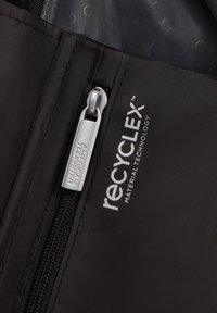Musta kangaskassi, jossa on sileä vetoketju hopeisella vetotapilla, ja logo-teksti "recycLEX™" sekä "AMERICAN TOURISTER" kohopainettuna sen viereen.