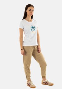 Camiseta blanca de manga corta con un diseño floral azul y lettering, combinada con pantalones jogger beige con bolsillos y dobladillos ajustados.