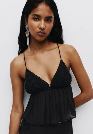 Black sleeveless top featuring a lace trim, a deep V-neck, and a flowing, layered hem. The fabric is lightweight with a soft texture.