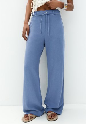 Pantalon large bleu clair en tissu doux, avec une taille à cordon et un ourlet effiloché. Associé avec des sandales beiges.
