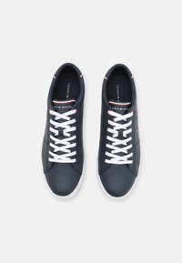 Ein Paar navyblaue Low-Top-Sneaker mit weißen Schnürsenkeln und Sohlen, die ein kleines Tommy Hilfiger-Logo auf der Zunge und an der Seite tragen.