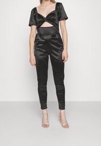 Mono de satén negro con mangas cortas abullonadas, sección media con corte y piernas ajustadas. Combinado con tacones plateados de tiras.