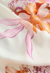 Látka s velkým, detailním květinovým potiskem v odstínech oranžové, růžové a fialové na hladkém, světlém pozadí.