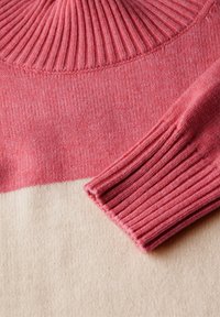 Stickad tröja med en ribbad krage i rosa och en beige nederdel. Mjuk textur och kontrasterande färgblock.