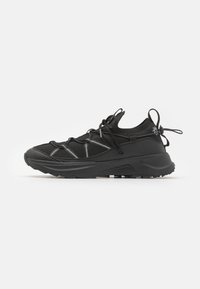 Baskets de sport noires avec une tige en mesh, des lignes d'accent gris et une semelle épaisse. Comprend des lacets élastiques et des languettes pour un enfilage facile.