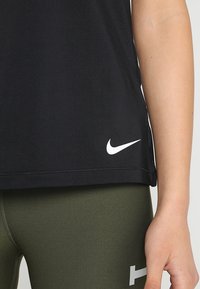 Černé sportovní tričko z měkké látky s bílým logem Nike na lemu, doplněné zelenými legínami se světle šedými detaily.