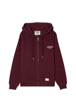 Sweat à zip bordeaux en tissu doux, avec une poche avant, une capuche à cordon de serrage et un logo brodé "Creeks" en doré.