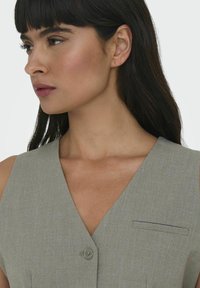 Grå skræddersyet kjole med V-udskæring, knapdetalje og en lille brystlomme. Glat stof med en subtil struktur.