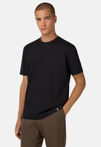Juodas medvilnės marškinėliai su apvaliu kaklu ir trumpomis rankovėmis, turintys minimalų siuvimą ir mažą logotipo etiketę apačioje.